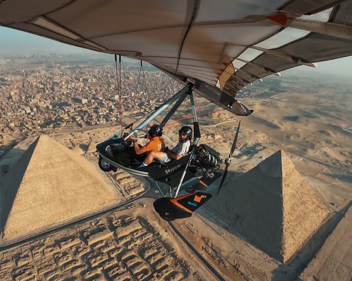 Microlight aircraft flying above the Pyramids of Giza with Cairo city in the background